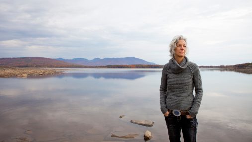 A woman looking out over the water on the shores of a calm lake.