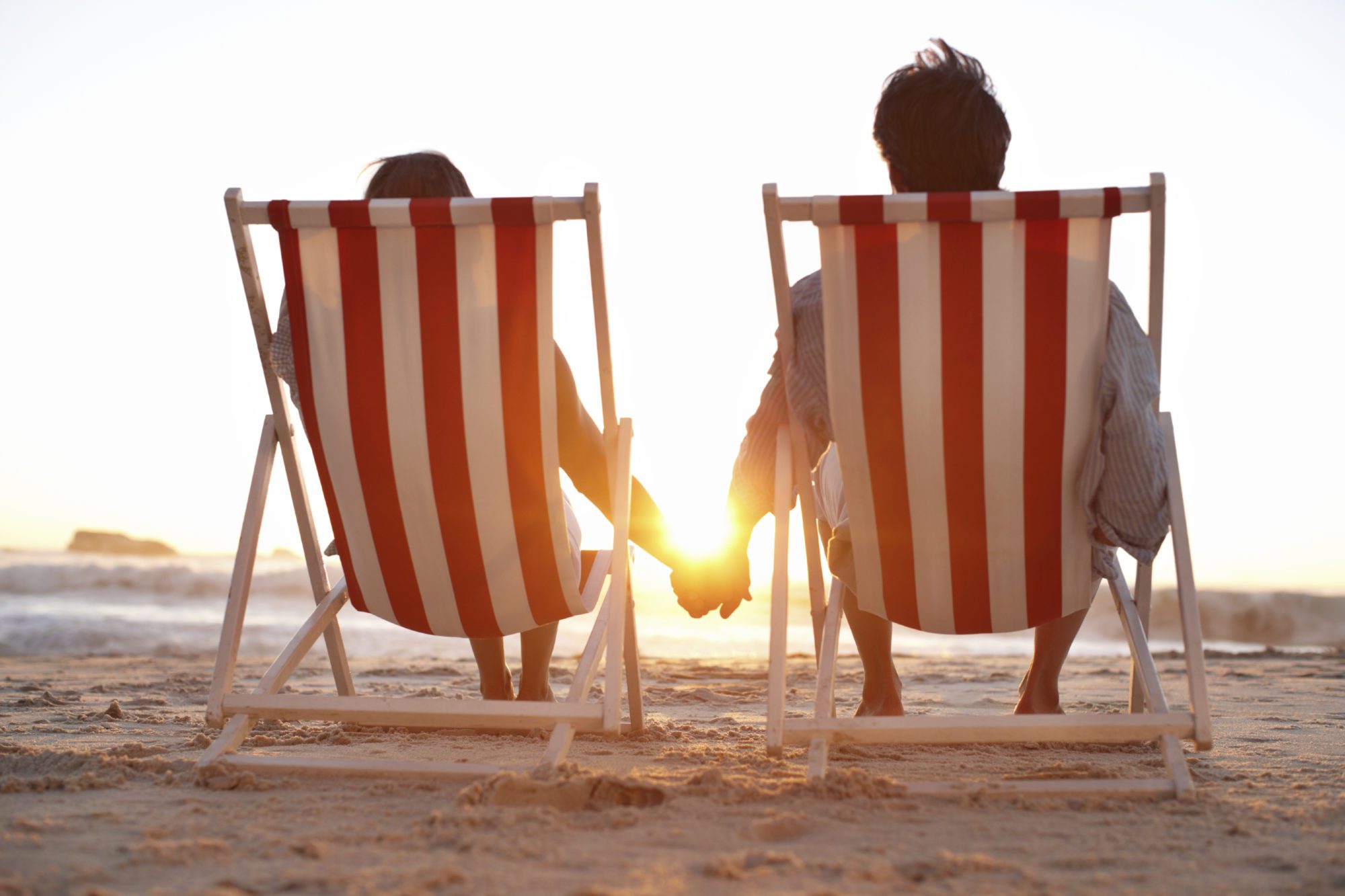 An affectionate couple sitting on the beach alongside copyspace during a pretty sunset